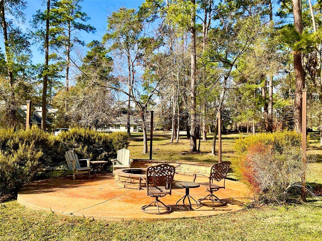 This backyard features a spacious patio with a fire pit and seating, surrounded by lush greenery and tall trees, offering a serene and inviting outdoor space for family or neighborhood friends.