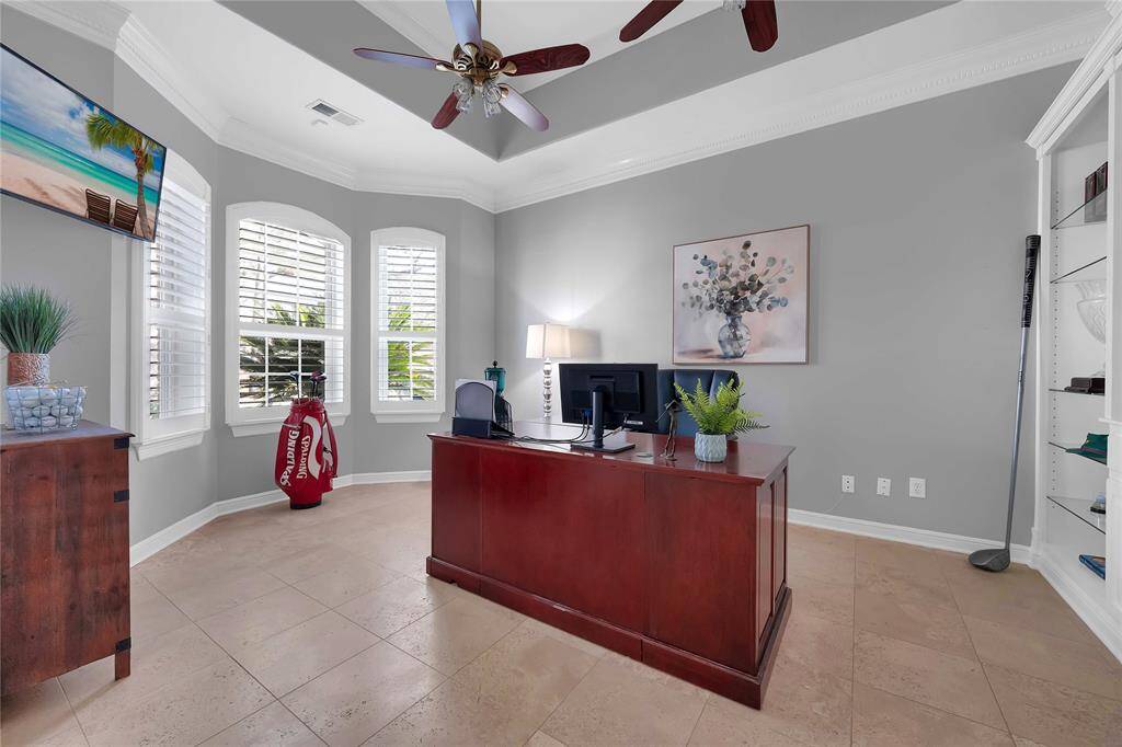 Spacious home office offers extensive built-ins with glass shelves, plantation shutters, coffered ceiling and travertine tile.