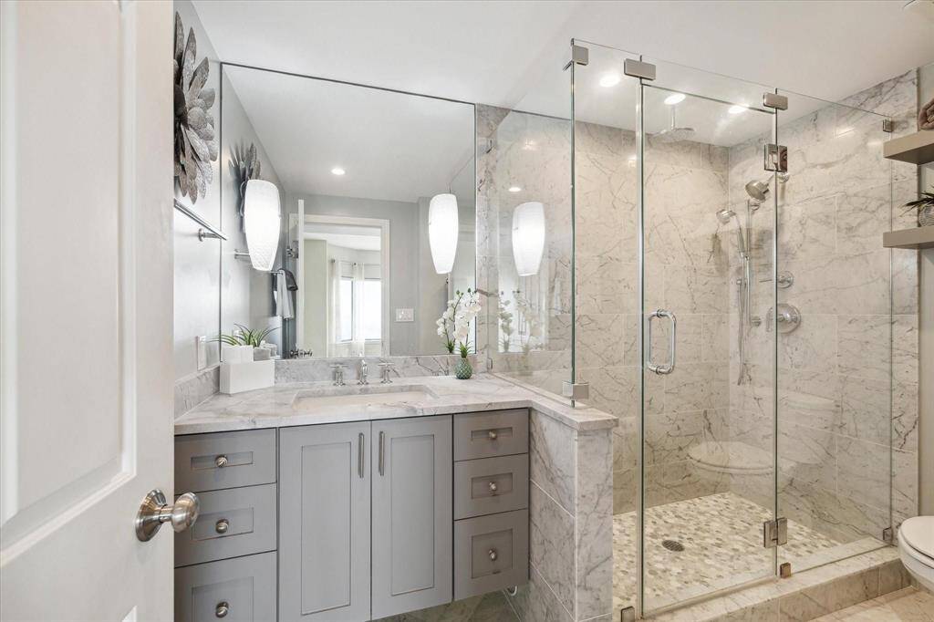 Primary Suite boasts a beautiful, upgraded en suite bathroom offering an oversized marble walk-in shower with frameless glass, marble topped vanity and floating shelves.