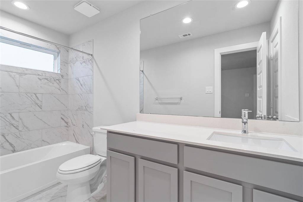 Secondary bath features tile flooring, bath/shower combo with tile surround, stained wood cabinets, beautiful light countertops, mirror, sleek fixtures and modern finishes.