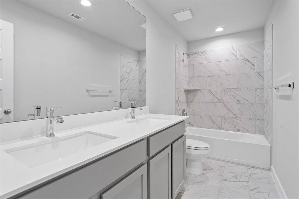 Secondary bath features tile flooring, bath/shower combo with tile surround, stained wood cabinets, beautiful light countertops, mirror, sleek fixtures and modern finishes.
