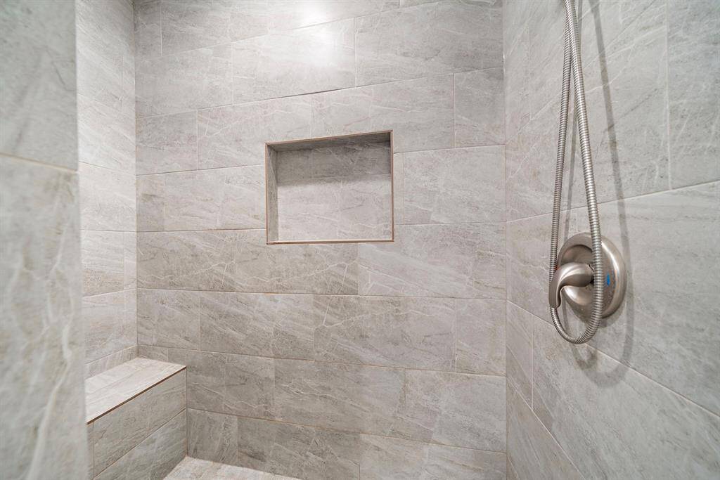 The oversized, fully tiled shower features a built-in bench and a recessed shelf for added convenience.