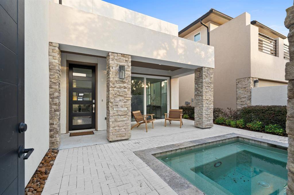 Contemporary and elegant home exterior featuring a beautifully designed front courtyard. The space is enhanced with modern architectural details, including textured stone columns that frame the entrance and patio area.