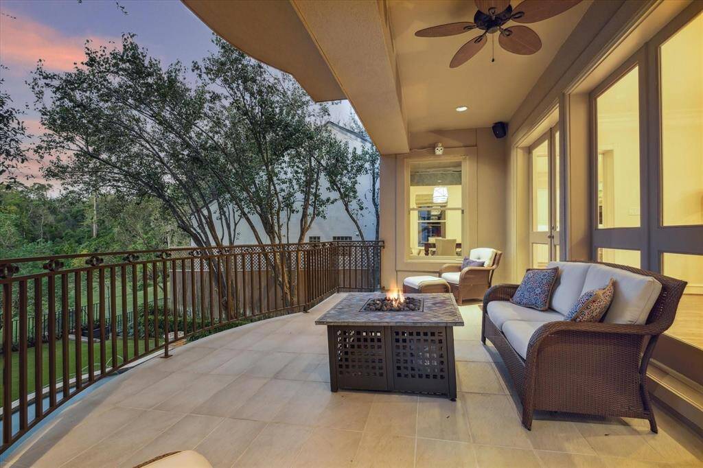 The luxurious family room centers around a gaslog fireplace with a custom stone mantle, flanked by built-in cabinetry featuring open shelving and custom back-lighting. French doors lead to a covered balcony, providing seamless indoor- outdoor living and entertaining.