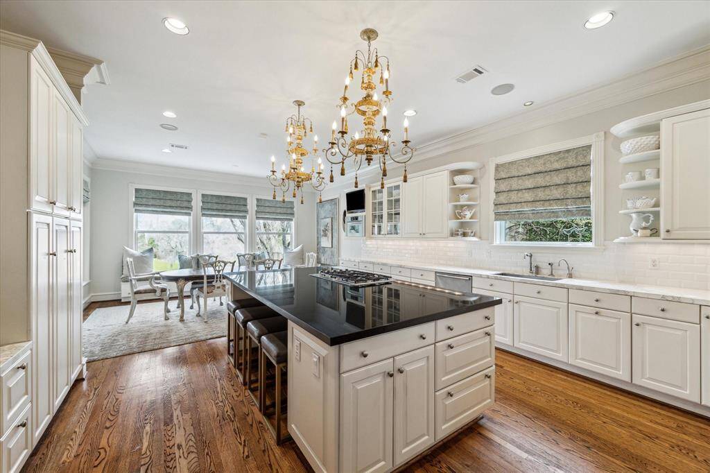 A stylish mini bar, complete with an ice maker, upper open shelving, and lower cabinetry, adds a touch of convenience and sophistication. Recessed LED lighting and an antique chandelier illuminate the space, while warm hardwood flooring, custom crown molding, and designer neutral wall paint create an inviting atmosphere.