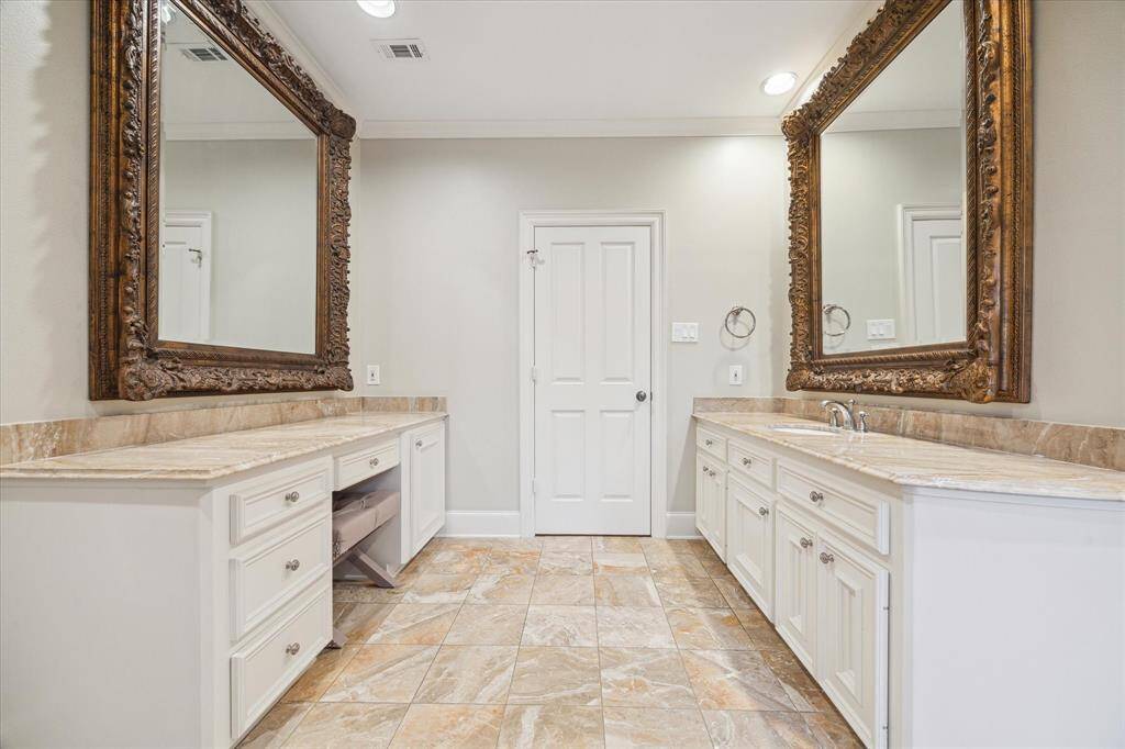 The elegant primary bathroom features marble tile flooring, custom crown molding, and designer neutral wall paint. A Passport Ensemble jetted tub and a walk-in shower with a steam function create a spa-like retreat. With marble countertops, a makeup vanity, recessed LED lighting, and two spacious primary closets—including a walk-in masterpiece with dual hanging levels, a packing island, and open shelving—this space blends luxury with functionality.