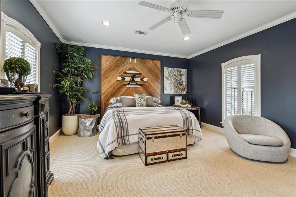 This luxurious secondary bedroom boasts dual windows offering serene views of the front lawn, framed by custom designer window treatments that add elegance to the space. Built- in shelving and a desk with knee space provide both functionality and style, while custom crown molding and recessed LED lighting enhance the room’s refined ambiance. The neutral carpet flooring and designer neutral wall paint create a cozy, sophisticated environment perfect for relaxation or study.