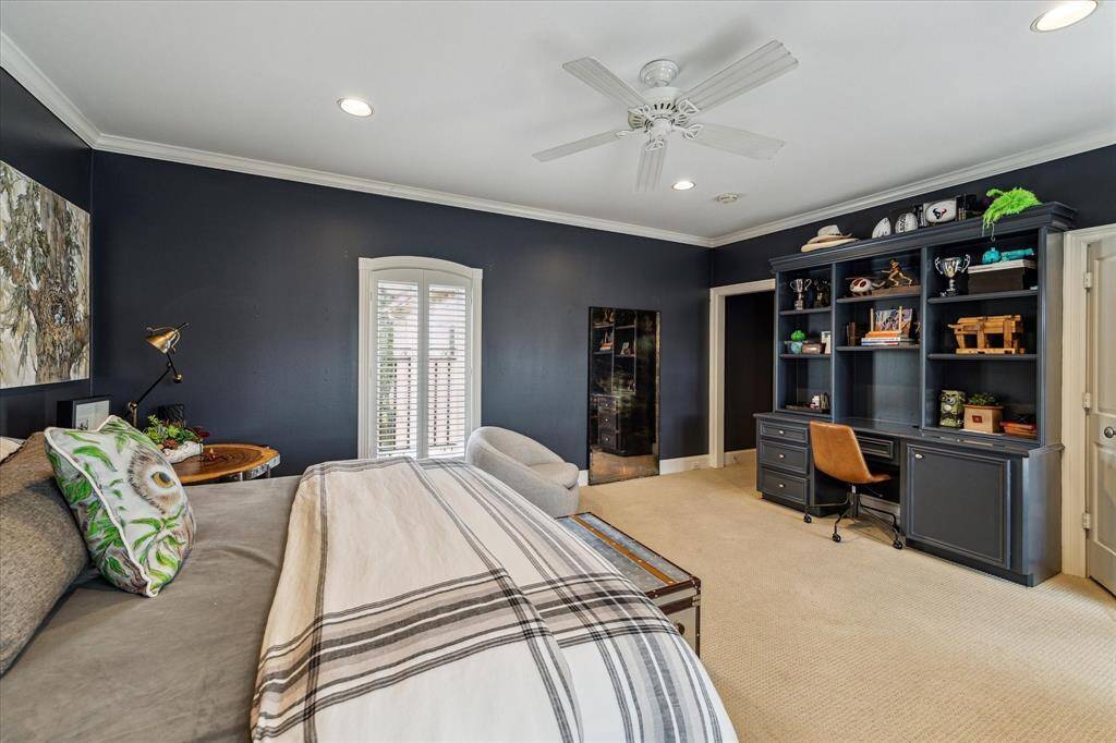This secondary bedroom boasts dual windows offering views of the front lawn and western exposures. Custom designer window treatments, a ceiling fan, and custom crown molding enhance the space’s elegance. Built-in shelving and a desk with knee space provide both functionality and style.