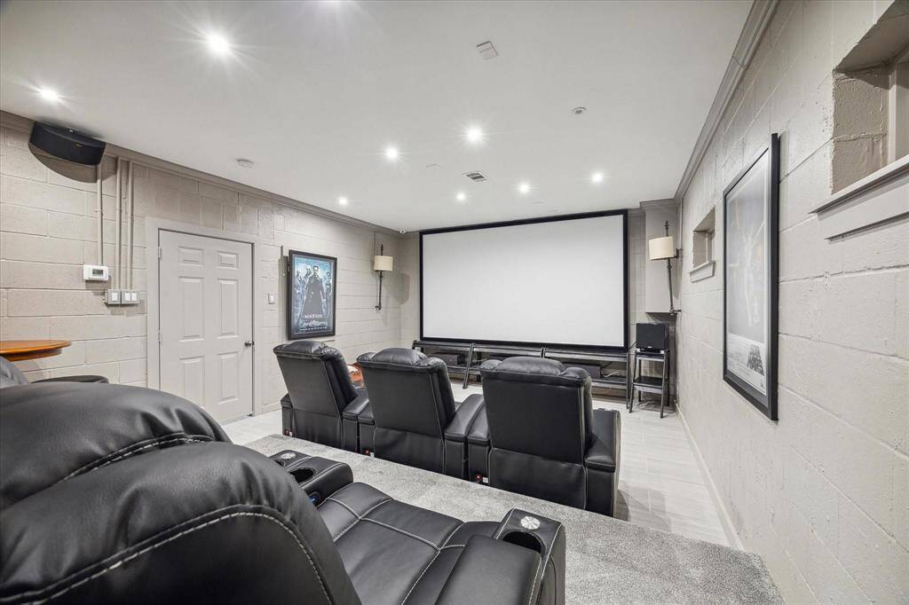 The luxurious media room features dual-level seating, a large viewing screen, and built-in speakers for an immersive experience. A trio of sconce lights adds ambiance, enhancing the theater-like atmosphere.