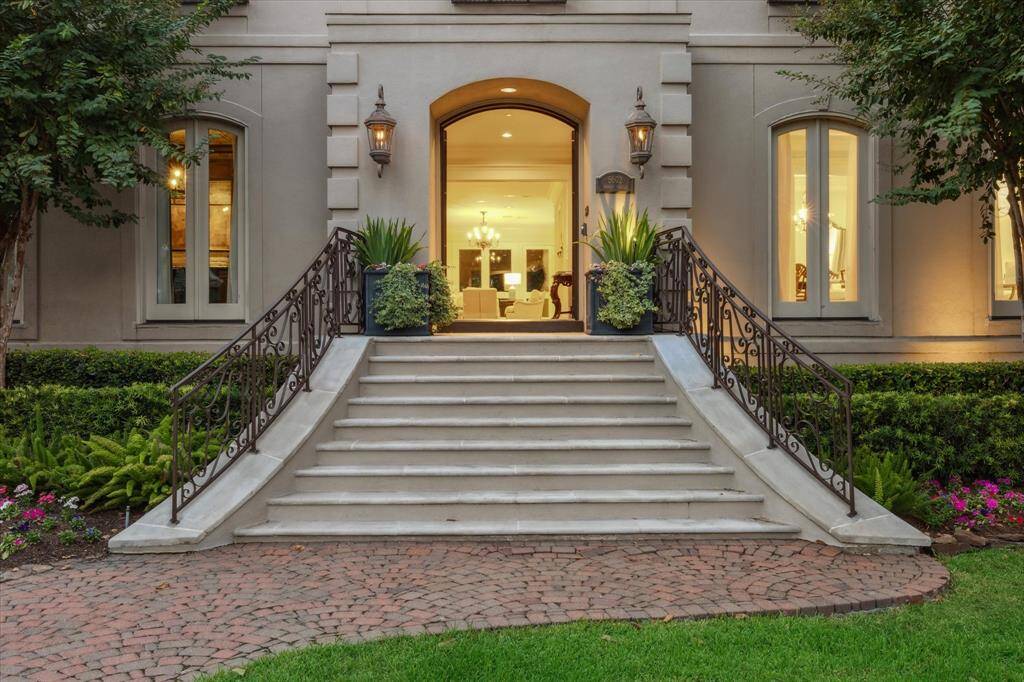 The grand entry of this luxury home features elegant steps leading to a stunning front door, flanked by dual lanterns that create a warm and inviting welcome. Fresh landscaping enhances the home's curb appeal, while expertly placed uplighting highlights the architectural beauty. This impressive entrance sets the tone for the sophistication found throughout the property.