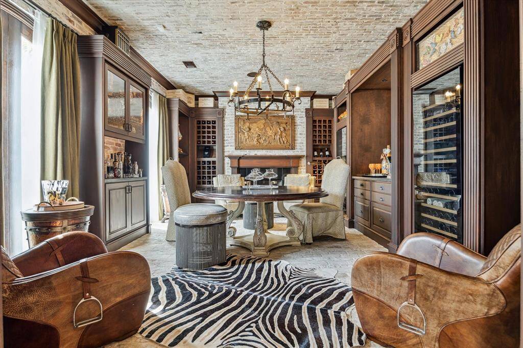 This elegant wine tasting room is a charming retreat, featuring antique brick floors and a matching ceiling, complemented by an antique iron chandelier. Dual windows with custom coverings offer serene views of the front lawn, while recessed LED lighting and custom crown molding elevate the room’s ambiance. Built-in stained wood cabinetry and open shelving provide ample space for showcasing your finest bottles and glassware.