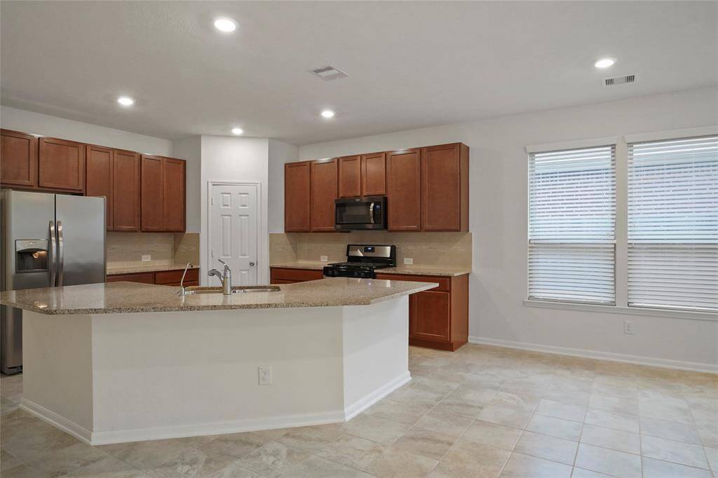 Close-up of the GIANT FLAT GRANITE Island for LOTS people, with a sink in back for convenience. Large Corner Pantry shows, + LOTS counter space, Stainless St. Frig to left, and gas cooking to right side at rear. Works really well as a 1 Butt Kitchen!