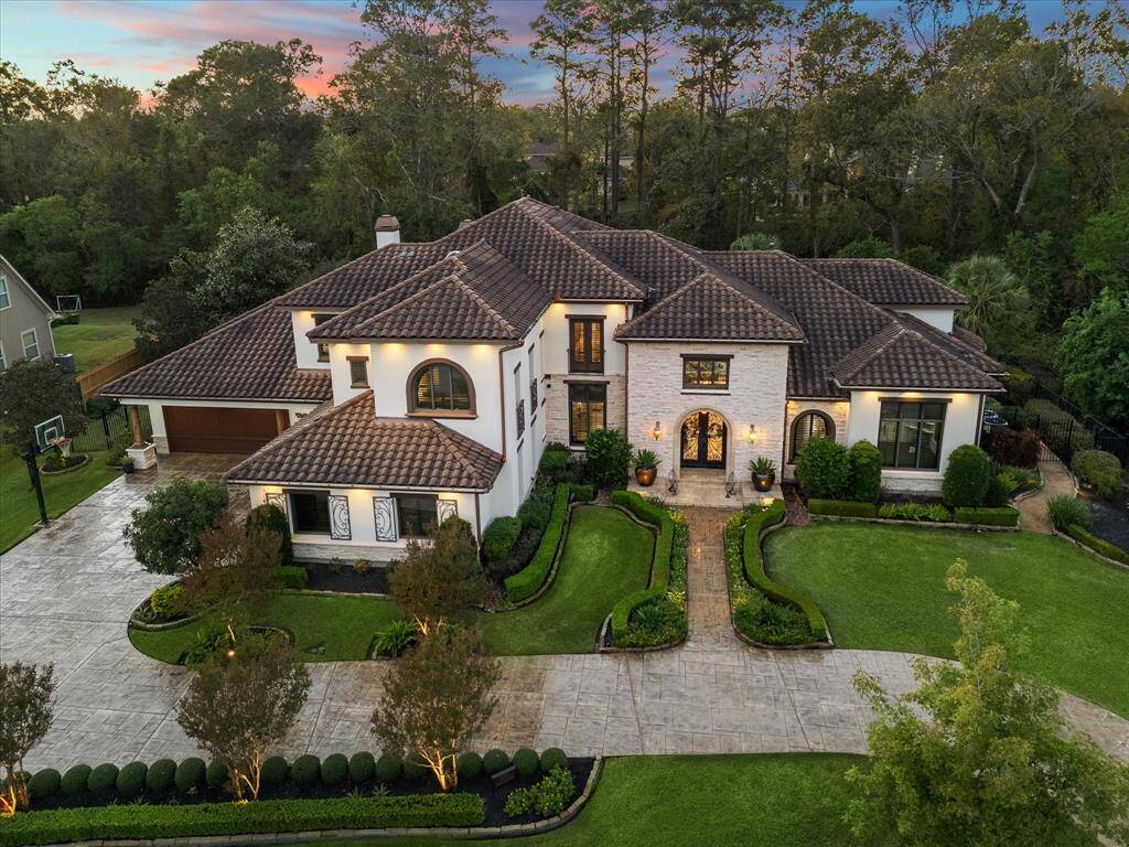 This is a luxurious two-story home with a well-manicured lawn and landscaping, featuring a tile roof, and an attached garage. The property is surrounded by mature trees, offering privacy and a serene environment.