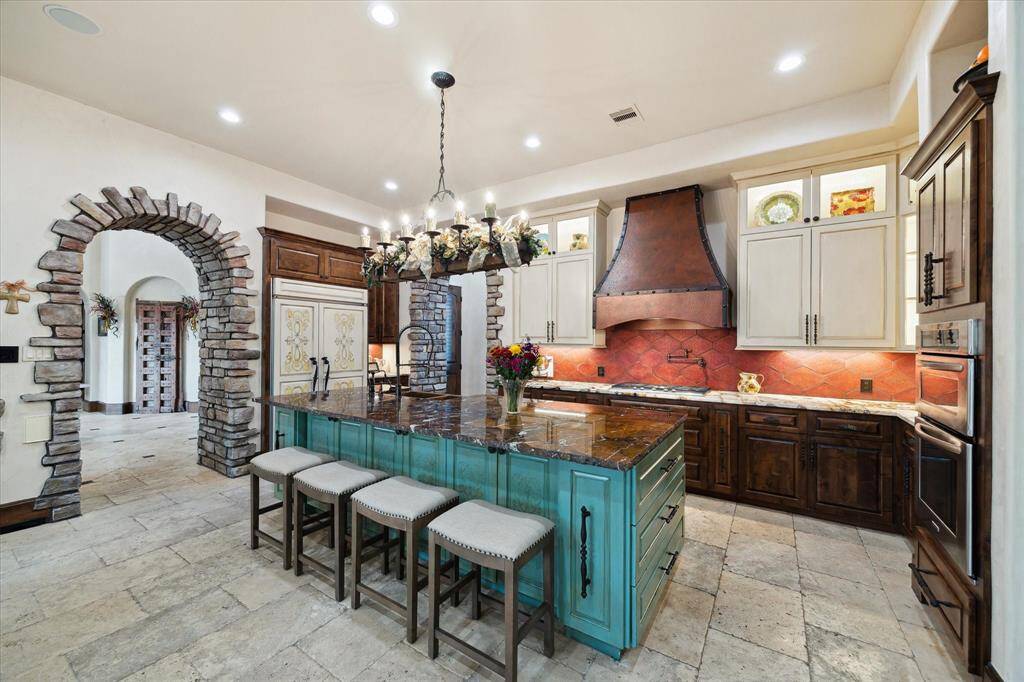 This spacious kitchen features a large central island with seating, extensive cabinetry, and high-end appliances, all complemented by elegant lighting and a warm color palette.