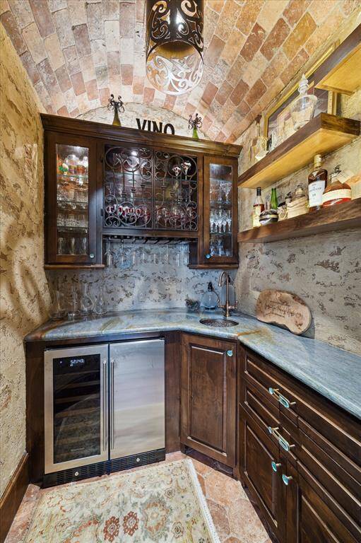This wine nook features a brick barrel ceiling, a built-in Knotty alder cabinetry with glass doors, a wine fridge, and  upscale countertops, perfect for entertaining and for wine enthusiasts.