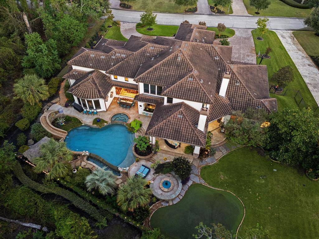 This is an aerial view of a luxurious, spacious home featuring a large custom pool with infinity edge and stone slide, pristine landscaping, and an attached 4 car garage. The property includes an award winning backyard with a putting green, offering a blend of leisure amenities and privacy.
