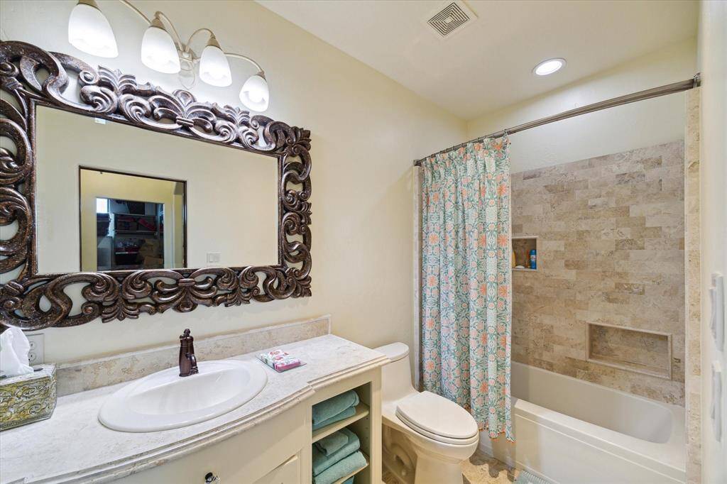 Another view of the bathroom with a single vanity, an ornate mirror, and a combined bathtub and shower with a tiled surround.