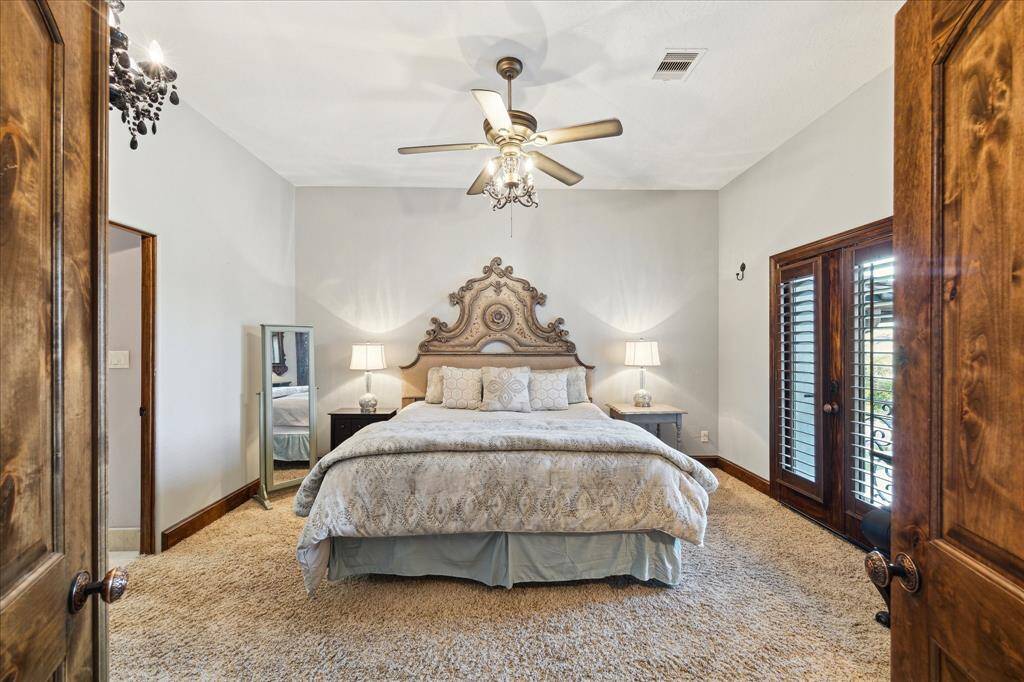 This is spacious, well-lit bedroom on the second floor featuring plush carpeting, a ceiling fan, elegant furnishings, and French doors leading to an exterior space.