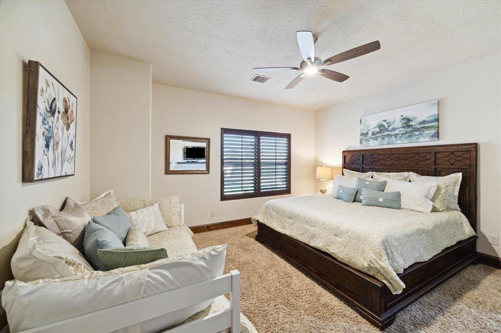 Another secondary well-lit bedroom featuring  a comfortable seating area, and tasteful wall art. The room is equipped with a modern ceiling fan and offers ample natural light through stylish window blinds.