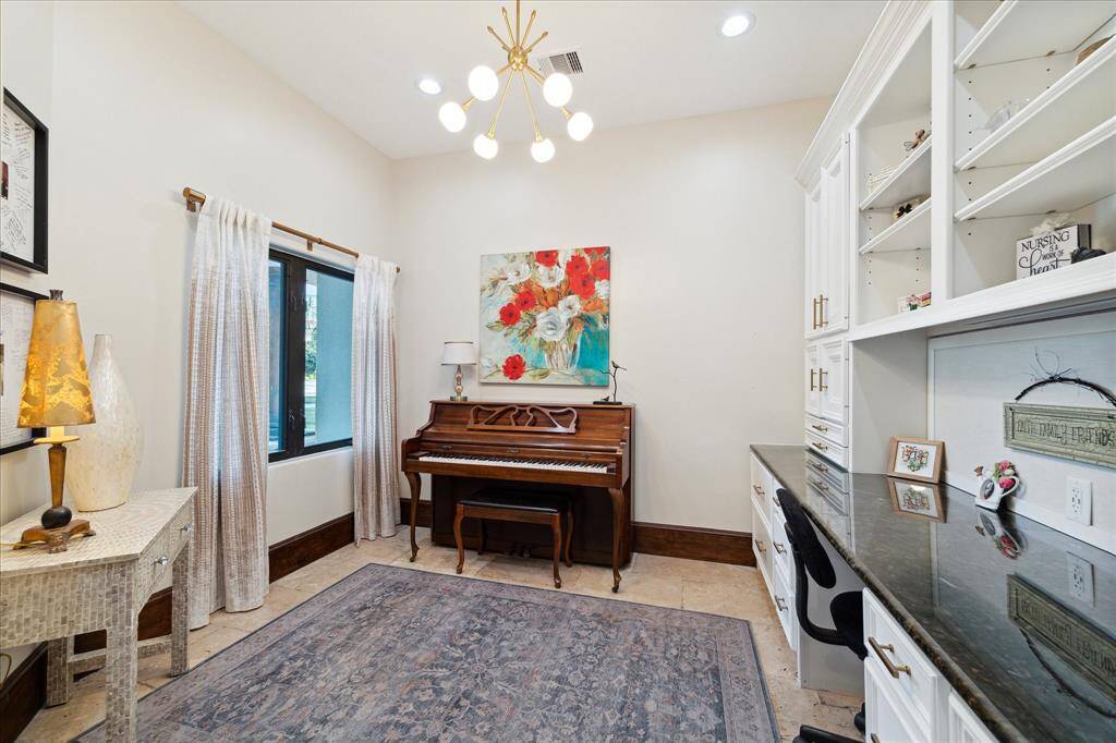 Bright and cozy room featuring a built-in desk with ample shelving, ideal for a home office or study. A piano against the wall suggests a creative space for music, and the room is complemented by a large window, elegant lighting, and hardwood flooring.