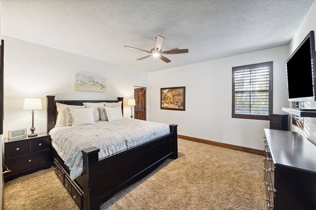This is a spacious secondary bedroom with a ceiling fan. The room has plush carpeting and a neutral color palette, with a window that allows for natural light.