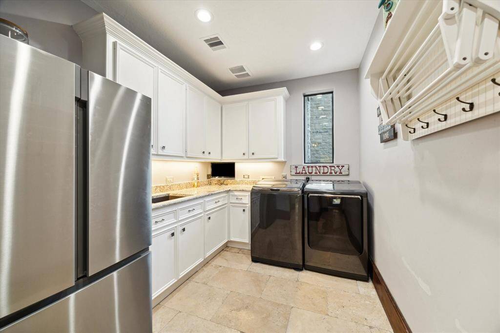 Modern and well-equipped laundry room featuring white cabinetry, granite countertops, stainless steel appliances, and a drying rack, complemented by tile flooring and a small window for natural light.
