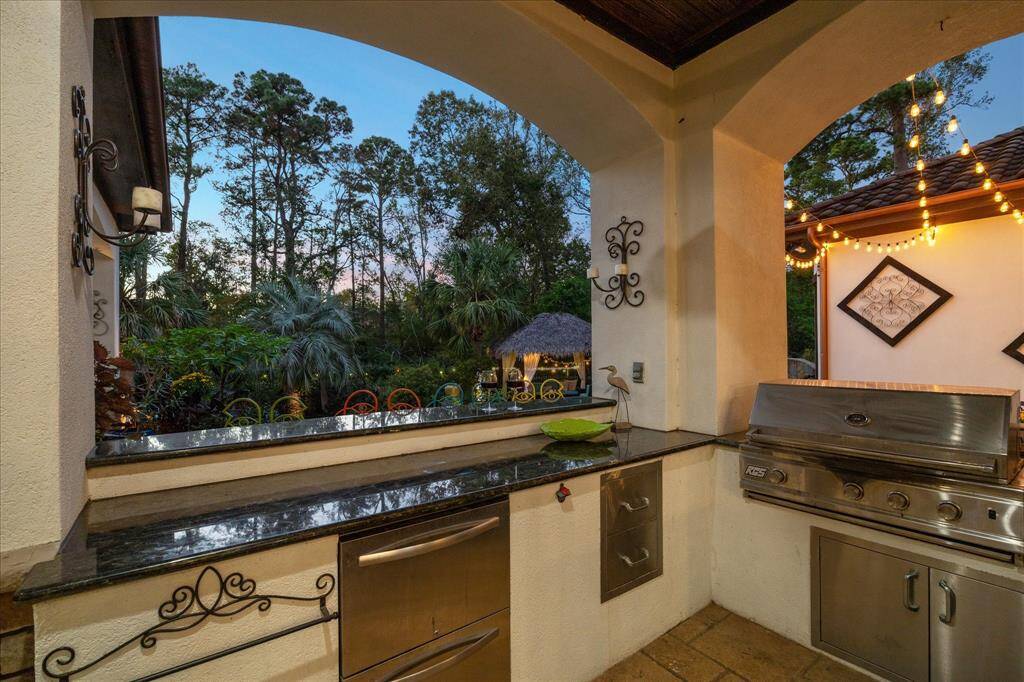 Outdoor kitchen with a built-in grill and storage, set against a tranquil backdrop of lush greenery and trees. Twinkling lights add a cozy atmosphere for evening entertaining.
