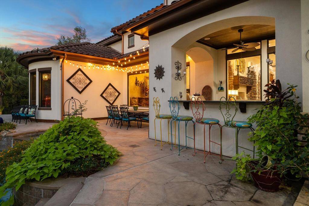 Charming outdoor patio area featuring a dining set, colorful bar stools, and decorative lighting, perfect for entertaining or relaxing in the evening ambiance.