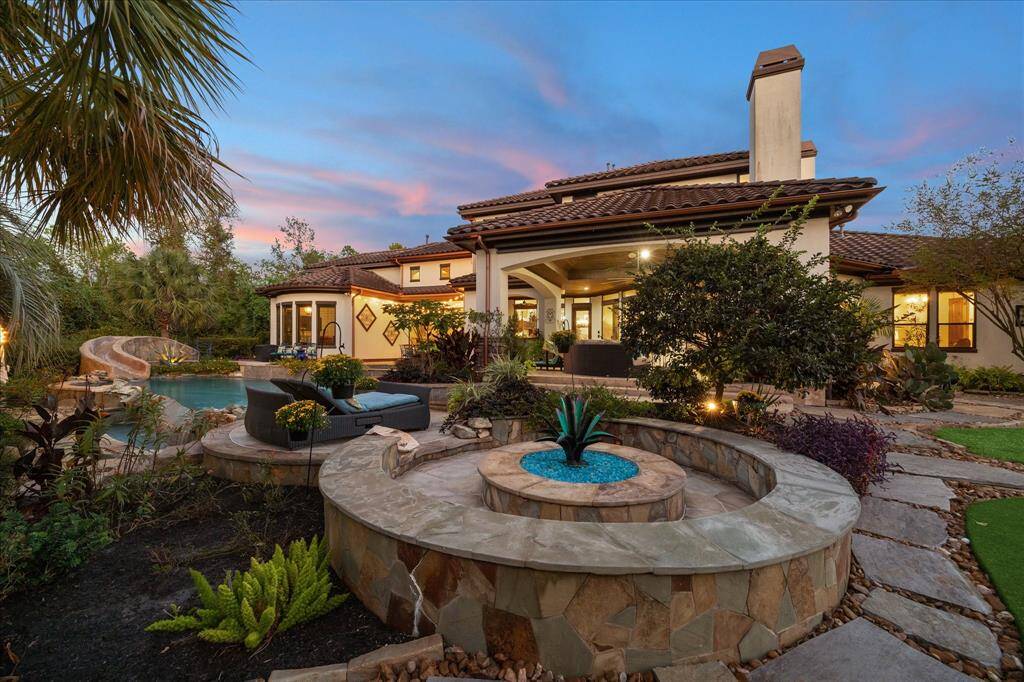 Relax in the beautifully landscaped backyard featuring a curved pool, a spa, and a fire pit area, perfect for entertaining. The architecture suggests a modern Mediterranean style with elegant outdoor lighting, offering a serene twilight ambiance.