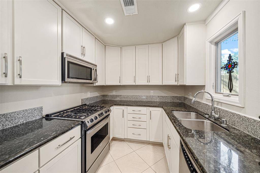 The kitchen boasts abundant storage, granite counters, gas oven and stove, and a built-in microwave with views into the backyard.