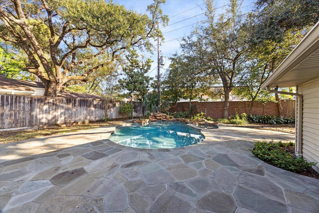 Pristine pool / spa with water feature sitting amongst a natural field stone patio partially shaded by mature oak trees.