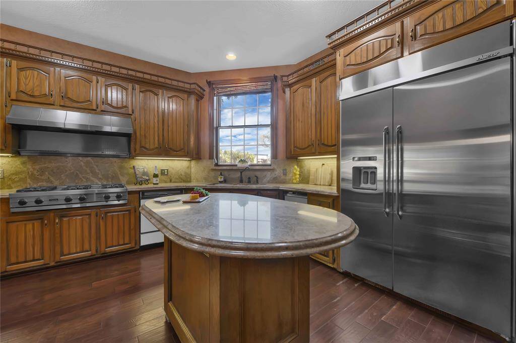 This is a spacious kitchen featuring rich wooden cabinetry, stainless steel appliances, a gas stove, and a central island.