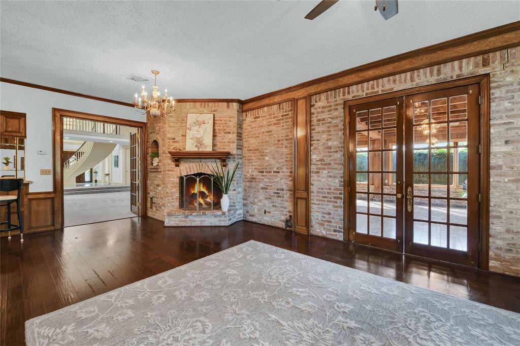 This room features a cozy fireplace with a brick surround, hardwood floors, large windows with garden views.