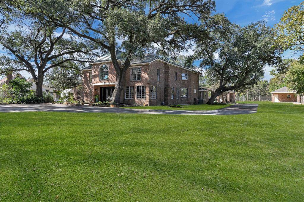 Grand entry offering ample shade and a serene setting. The property includes a wide driveway leading to a detached garage.