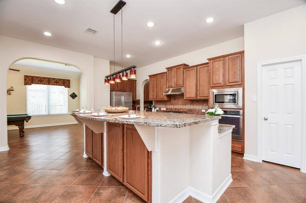 This spacious kitchen features elegant granite countertops, warm wood cabinetry, and modern stainless steel appliances. The open design flows into a bright adjacent room, ideal for entertaining.