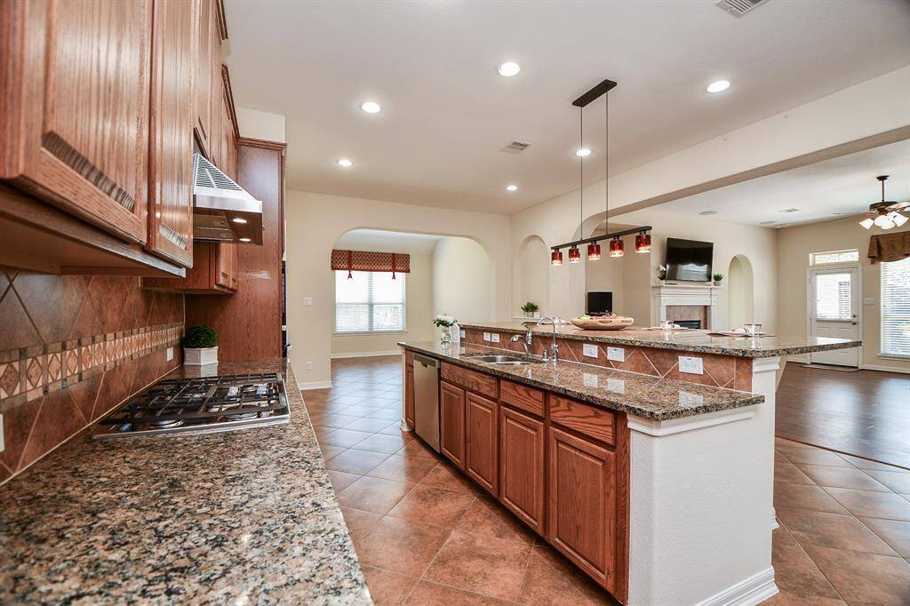 This spacious kitchen features granite countertops, a large island with a sink, and a gas stove. It opens to a bright living area with a cozy fireplace, offering an inviting and functional space for entertaining.