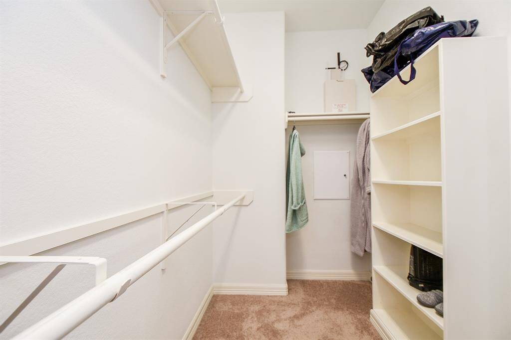 This is a spacious walk-in closet with ample shelving and hanging space, featuring neutral carpeting and a clean, organized layout.