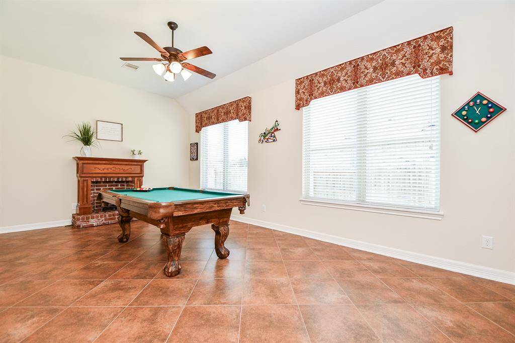 This bright room large enough for a pool table, tiled flooring, and large windows with patterned valances. A ceiling fan provides comfort, making it an ideal recreational space.