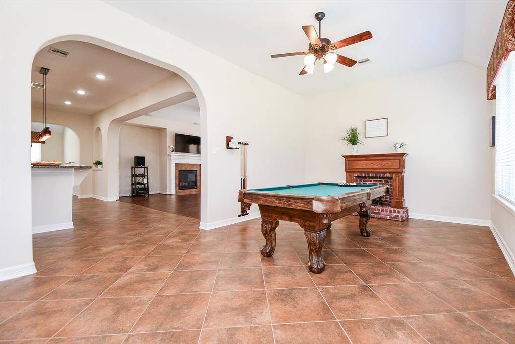This spacious room features elegant tile flooring and ideal for entertainment. It includes a ceiling fan, and arched doorways leading to an open-concept living area with a cozy fireplace. Natural light streams in through large windows, creating a warm and inviting atmosphere.
