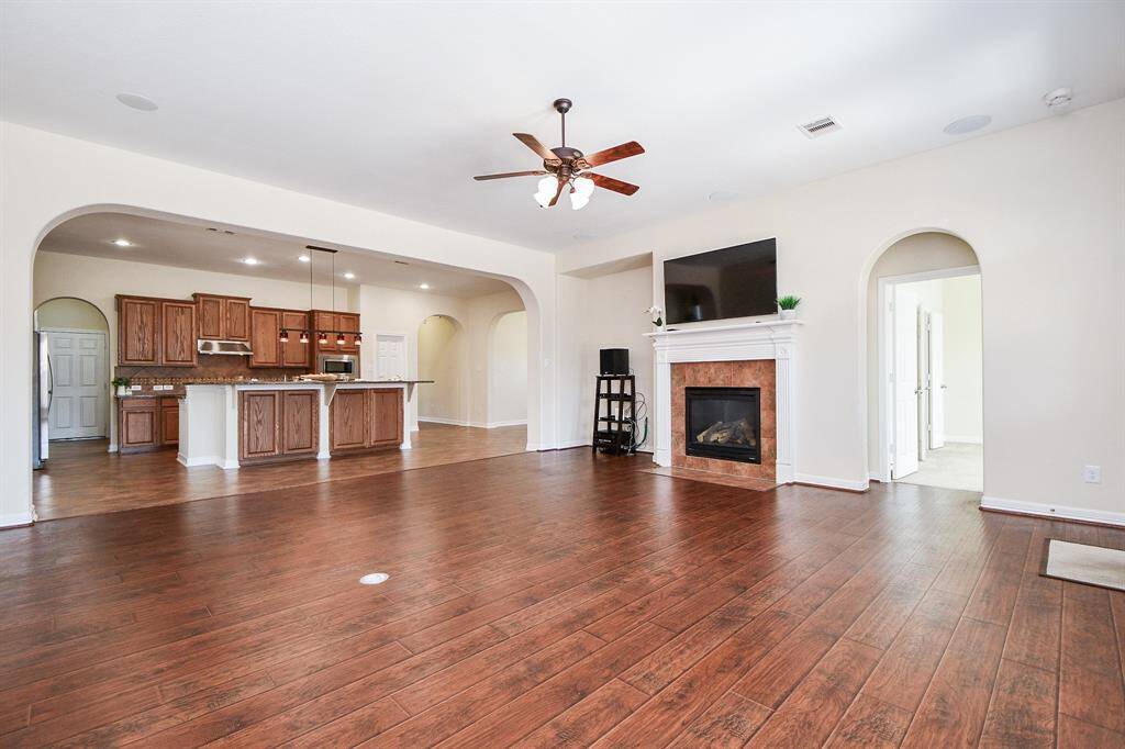 This spacious open-concept living area features hardwood floors, a cozy fireplace, and a ceiling fan. The kitchen boasts wooden cabinetry, a large island with bar seating, and modern appliances, perfect for entertaining or family gatherings.