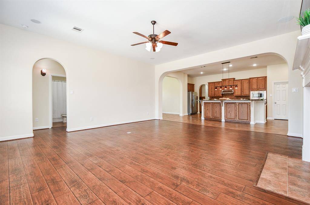 Spacious open-concept living area with hardwood floors, ceiling fan, and archways. The kitchen features wooden cabinetry, granite countertops, and modern appliances. Ideal for entertaining and family living.