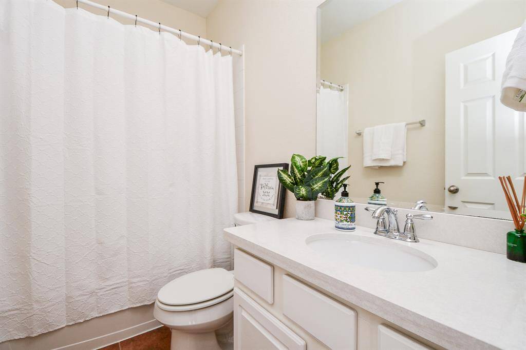This bathroom features a clean, modern design with a white vanity, sleek fixtures, and a neutral color palette. The space includes a shower with a curtain, a large mirror, and tasteful decor, creating a bright and inviting atmosphere.