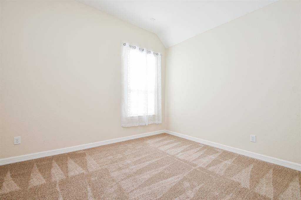 This is a bright, neutral-colored room with carpeted flooring and a single window with sheer curtains, providing natural light. Perfect as a bedroom or home office.