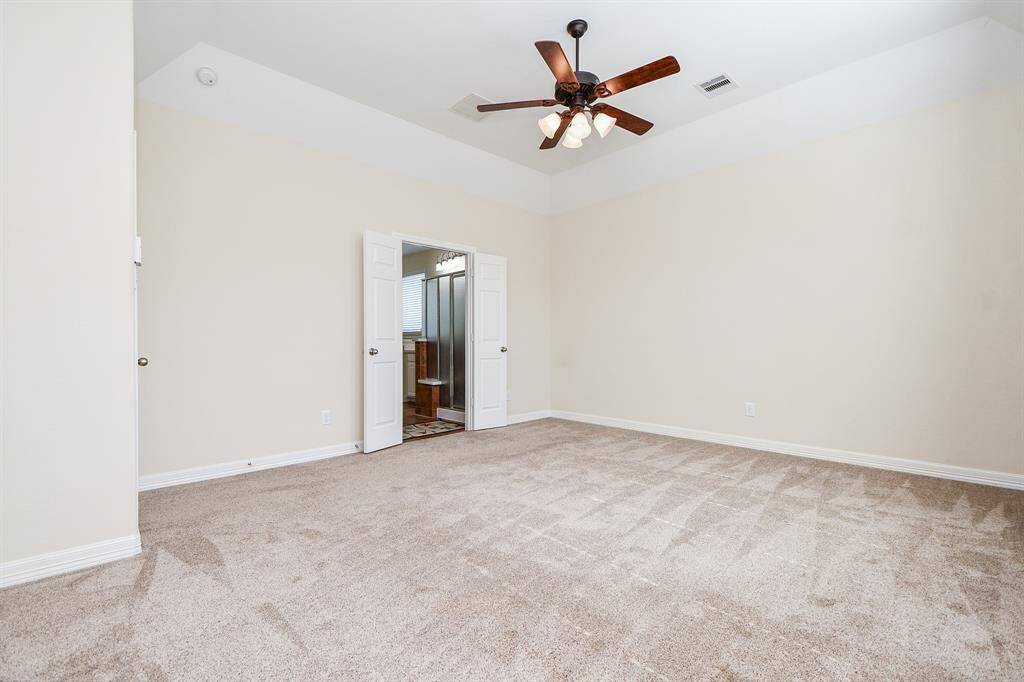 A spacious, carpeted bedroom with neutral walls, a ceiling fan, and double doors leading to an adjoining room or bathroom.