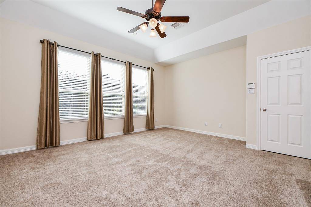 This spacious, well-lit room features neutral carpeting, a ceiling fan, and three large windows with elegant curtains, providing a cozy and inviting atmosphere.
