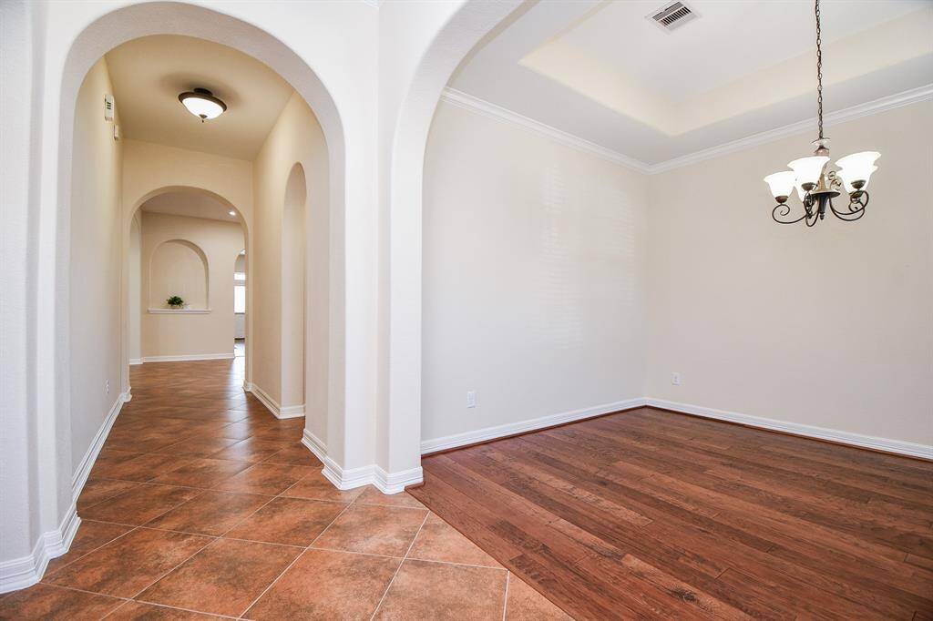 This photo showcases a bright, welcoming hallway with tiled flooring, featuring elegant archways leading to different areas. Adjacent is a room with wood flooring, crown molding, and a stylish chandelier, perfect for dining or as a formal sitting area.