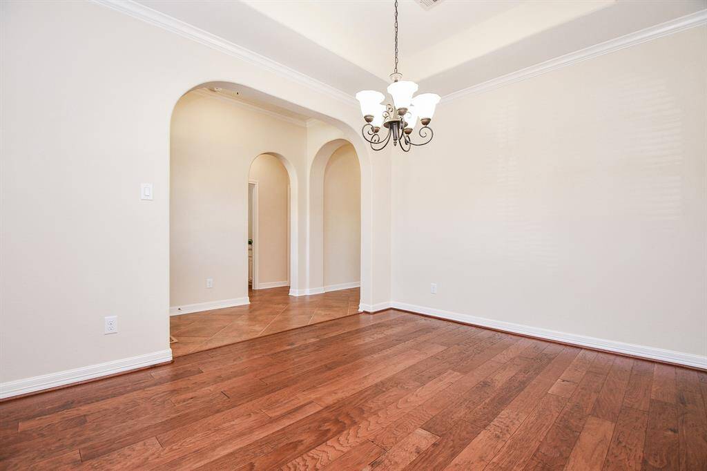 This photo showcases a spacious room with warm hardwood flooring and soft beige walls. It features elegant arched doorways and a stylish chandelier, creating a classic and inviting atmosphere.