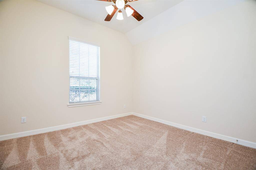 This room features a neutral color palette with a soft carpet, a large window for natural light, and a ceiling fan for comfort. Ideal for a bedroom or office space.