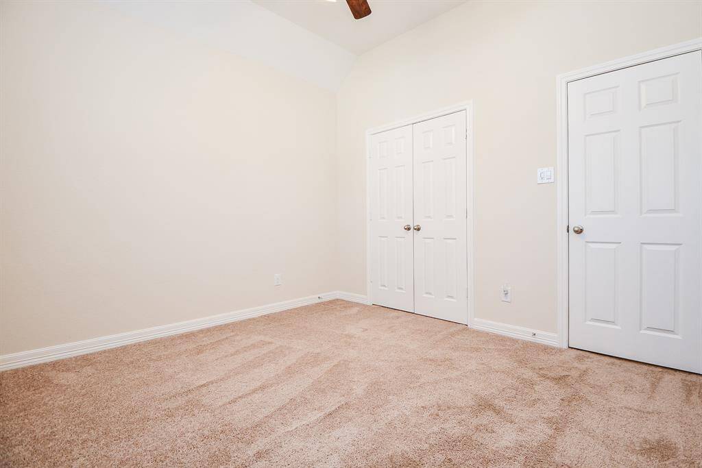 This room features neutral walls, plush carpet, a ceiling fan, and double doors leading to a closet, providing a cozy and functional space.