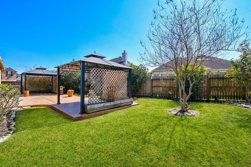 This backyard features a well-maintained lawn, two elegant gazebos with lattice detailing, and a wooden fence for privacy. Ideal for outdoor entertaining and relaxation.